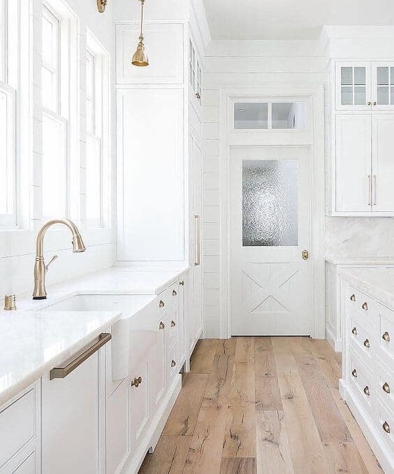 Modern Farmhouse white kitchen cabinets and sink with brass hardware and fixtures natural light wood plank flooring