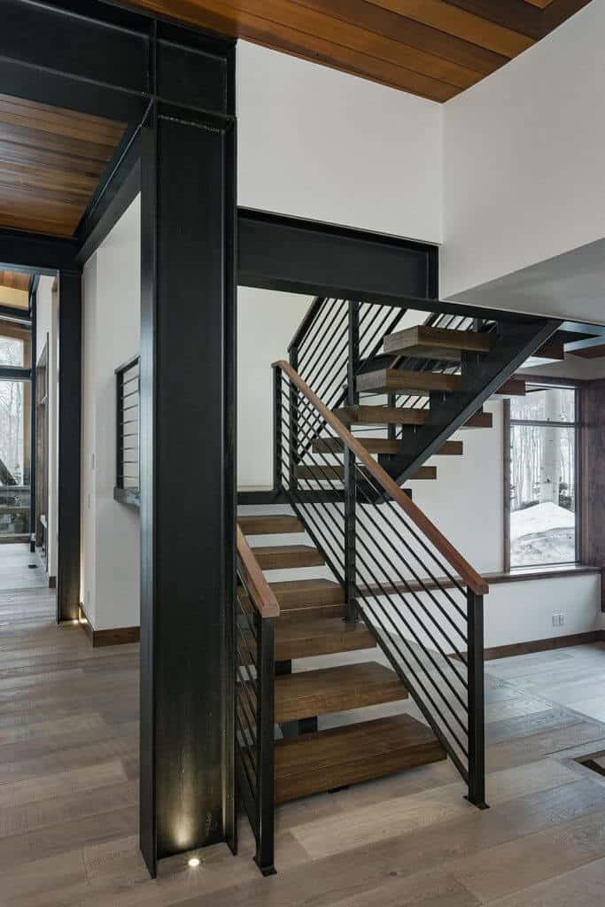 modern floating staircase with wood open treads and a single central metal stringer. has metal railing with top wooden rail. c channel beams supports second floor and add industrial feel to this mountain home