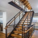 A modern open tread staircase with natural colored wood treads and black steel beam stringers provide access to the second and basement floors. Railing is a combination of metal, wood and cable system.