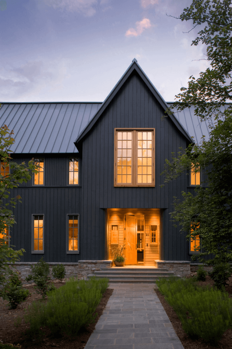 A dramatic dark modern farmhouse with board and batten siding and tan windows with grids. The steep pitch to the gable and steel roof add the finishing touches to this modern exterior. #downleahslane #darkhouse #exteriordesigns #exteriorideas #blackhouse #blackexterior #blackhome #modernfarmhouse #tanwindows #steelroof #modernexterior
