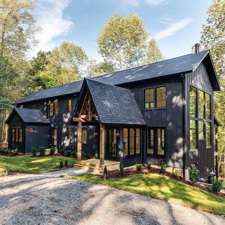 A gorgeous dark modern farmhouse exterior with contrasting natural wood in a dramatic pitched roof entryway make this home a showstopper! Home by Carbine & Associates. #downleahslane #blackhouse #blackhome #darkexterior #darkhouse #entryway #coveredporch #customhome #luxuryhouse #dreamhome #vaultedceiling