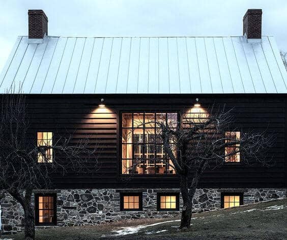 A dramatic black exterior with natural stone basement topped with a light steel roof provides great contrast and appeal to this home. #downleahslane #darkhouse #blackhouse #darkexterior #stonefoundation #steelroof #exteriorcolor