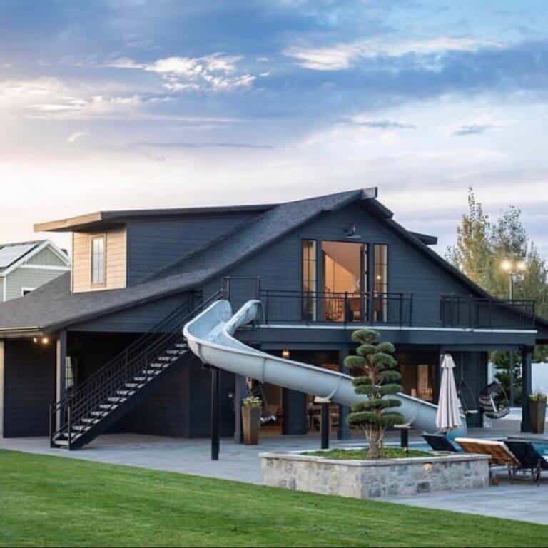 Black exterior on a pool house that was once a barn. Slide coming off second floor swirls down to the pool. Japanese tree adds landscape interest.